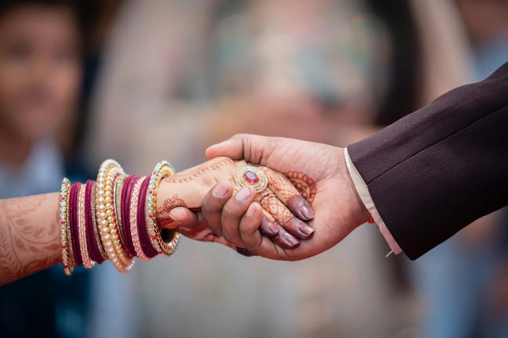 Close-up of a couple holding hands adorned with henna and bangles, symbolizing unity.